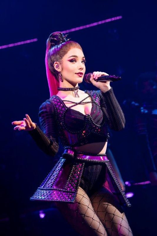 A person wearing a black and pink outfit sings on stage.