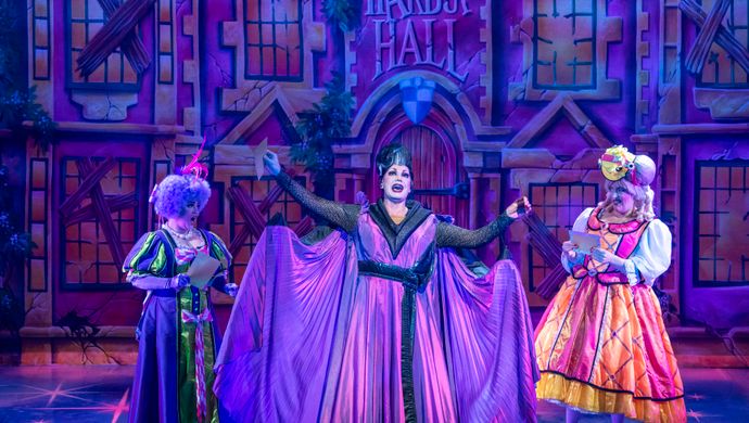 The Wicked Stepmother stands centre stage in a purple dress and cape.