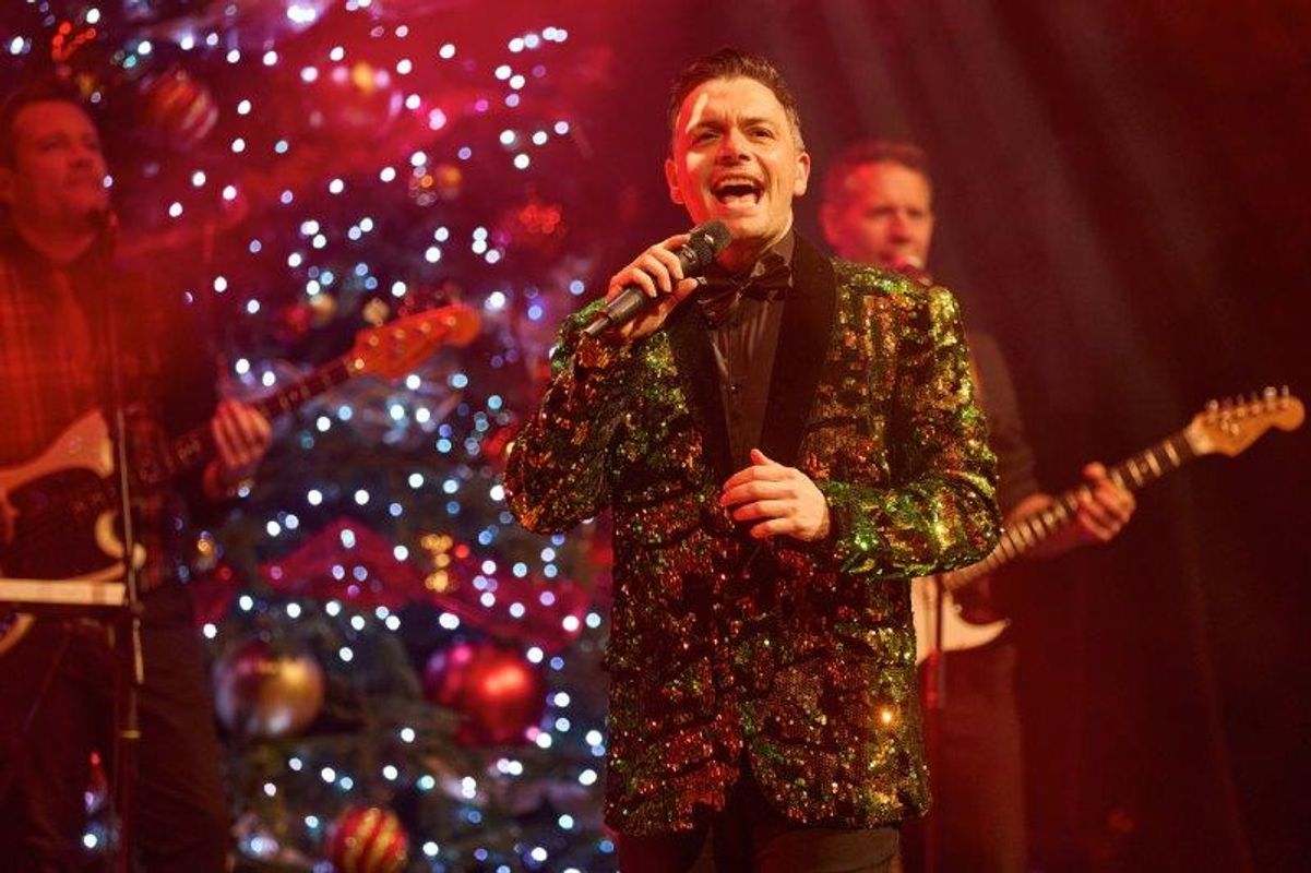 A singer wears a dark sequined blazer onstage.