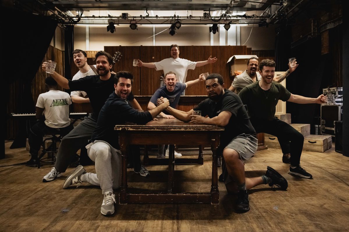 Group on men in a pub like setting, dancing and singing