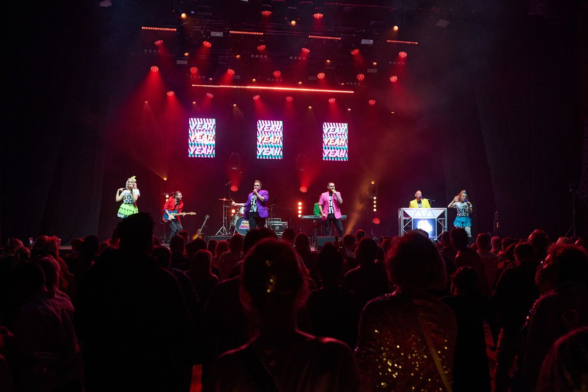 An audience watches five performers singing on stage.