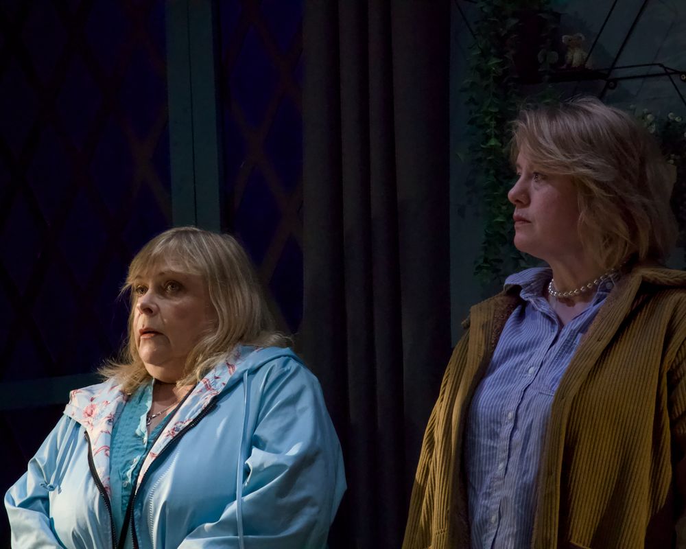 Two people stood together in a dimly lit room. One has a worried look on their face