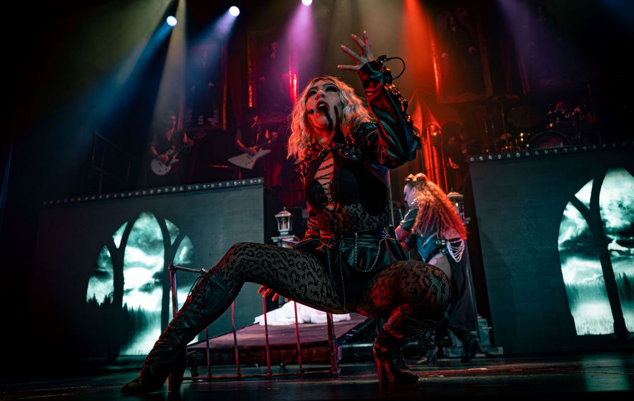 A person in a sitting position sings whilst raising their left hand.