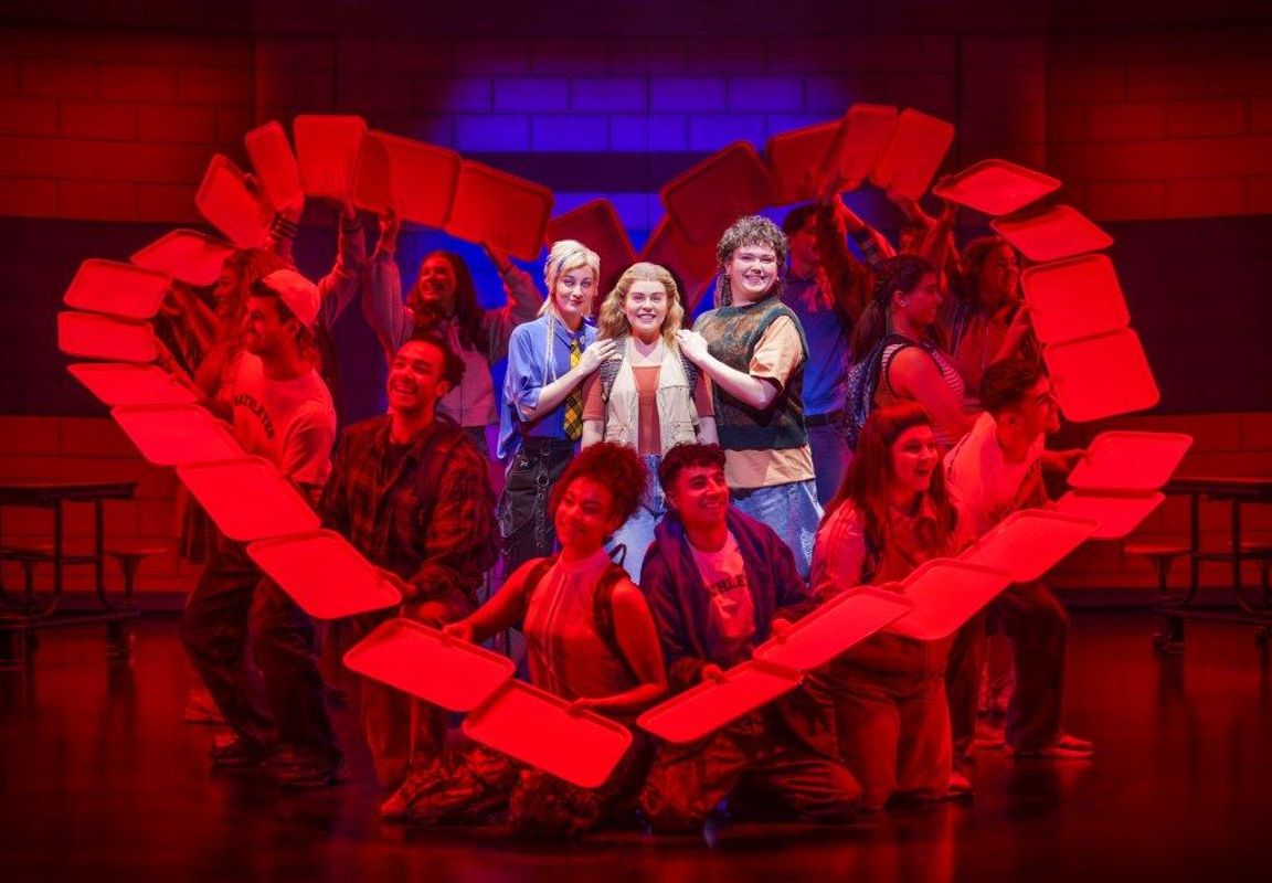 Three people in the centre of a red heart made of paper that others are holding up around them