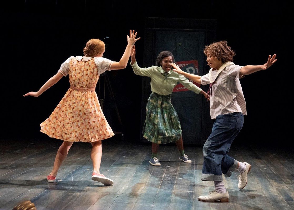 Three people are dancing in a circle together. They appear to be in 1940s style clothes