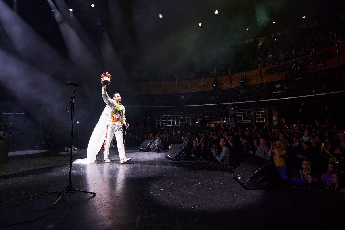 A man on stage wearing a long white cape and holding a crown