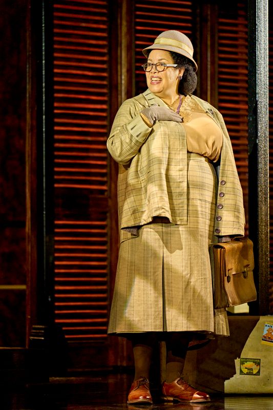 A person dressed in a checked skirt suit has their hand on their chest.