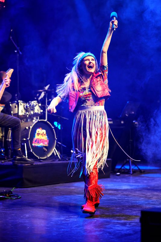 A person wearing a blue bandana and red leather jacket raises their right arm in the air..