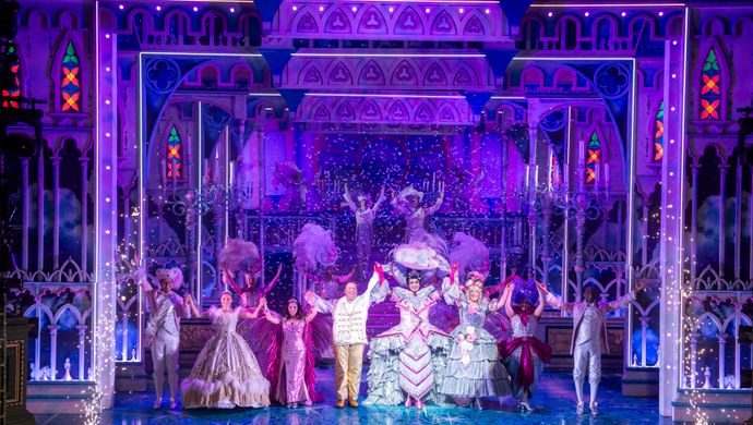 The Cinderella company stand centre stage with  their arms above their heads.