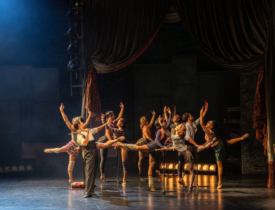 An ensemble of dancers on stage with their legs and arms outstretched.