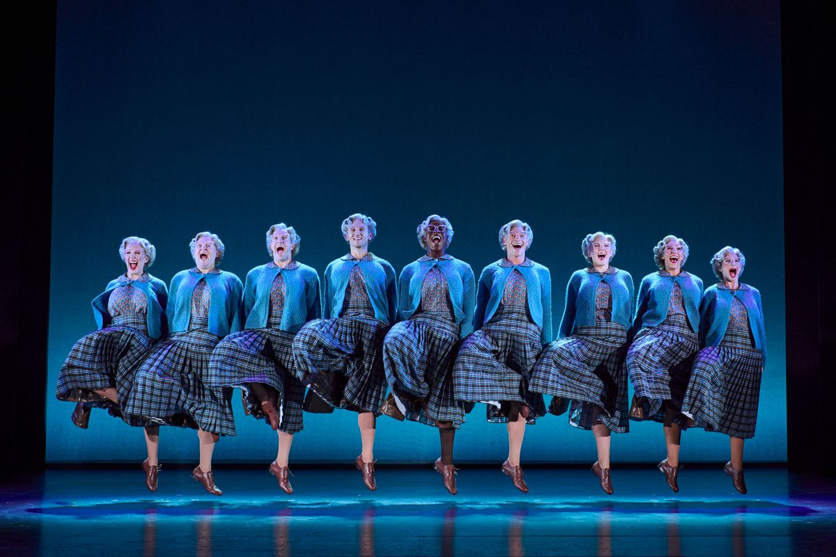 An ensemble stand in a conga line all dressed as Mrs Doubtfire.