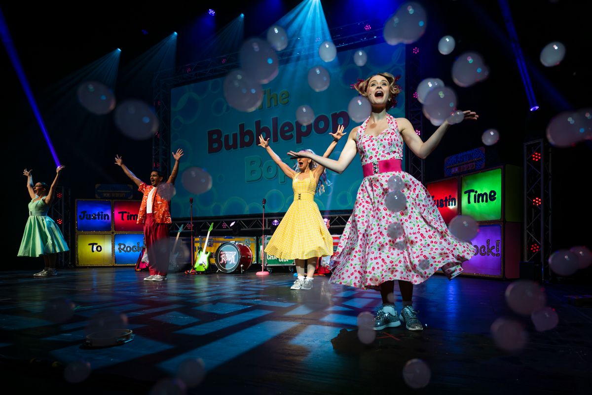 The ensemble members dance with their arms outstretched. 