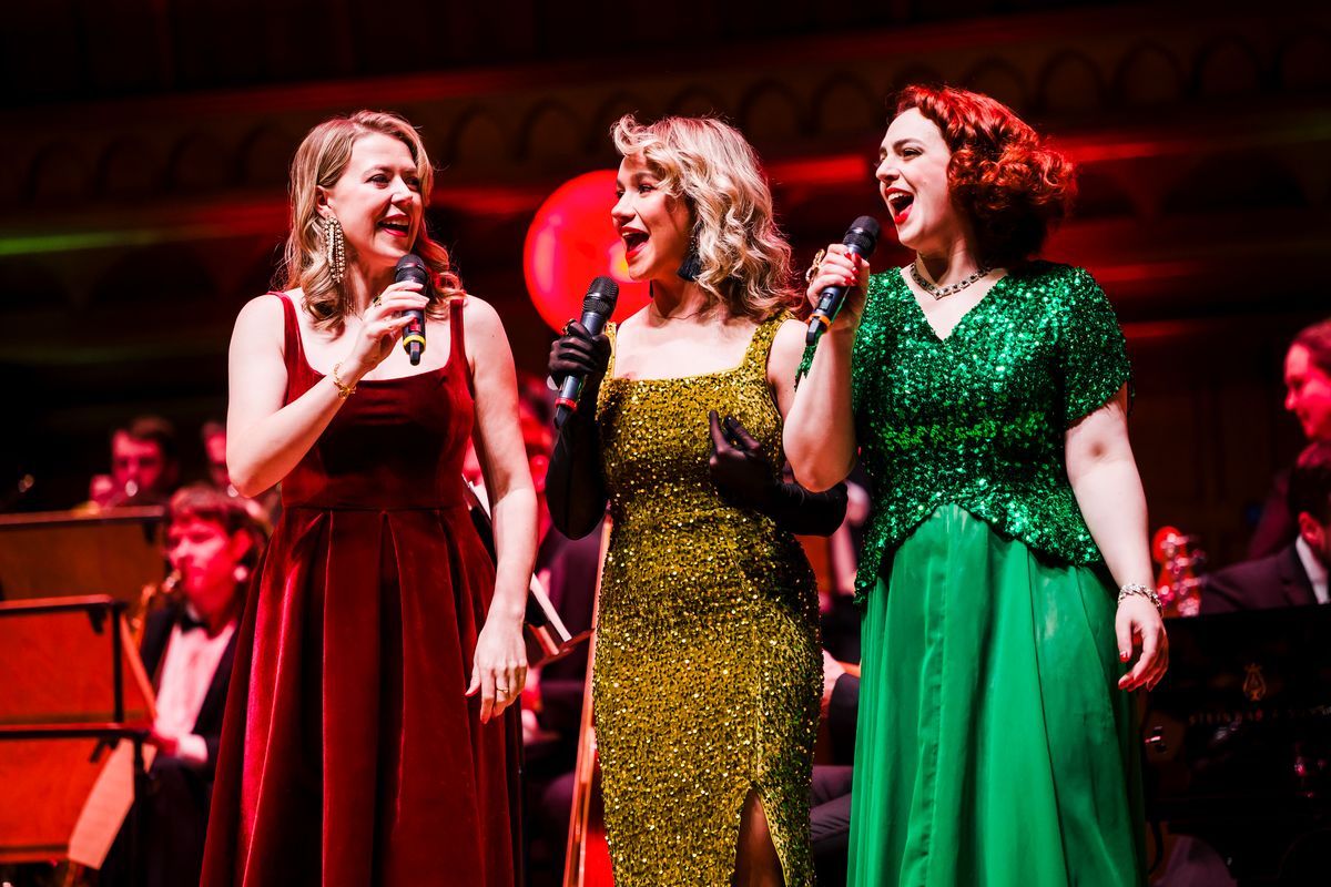 Three people dressed in long brightly coloured dresses sing.