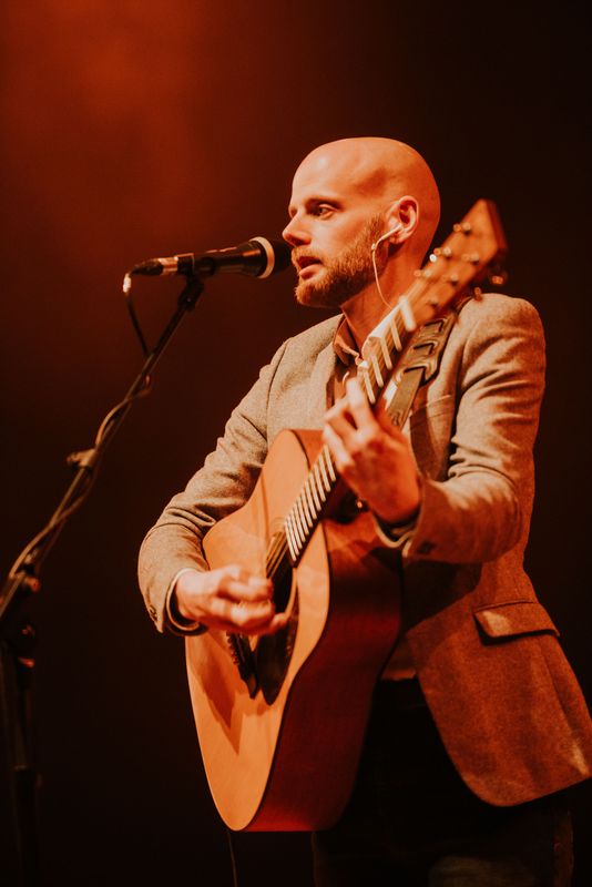 Person singing into a microphone and playing the guitar