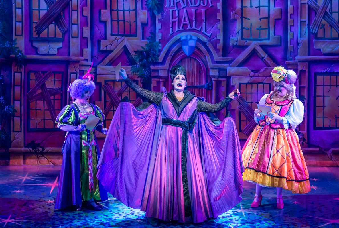 The Wicked Stepmother stands centre stage in a purple dress and cape.