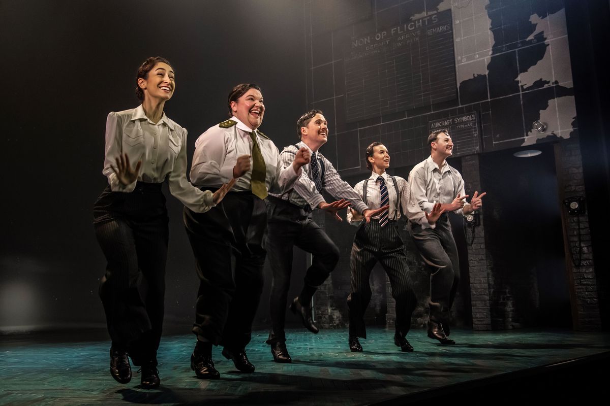 Five people stood in a row  all wearing white shirts, ties and black trousers
