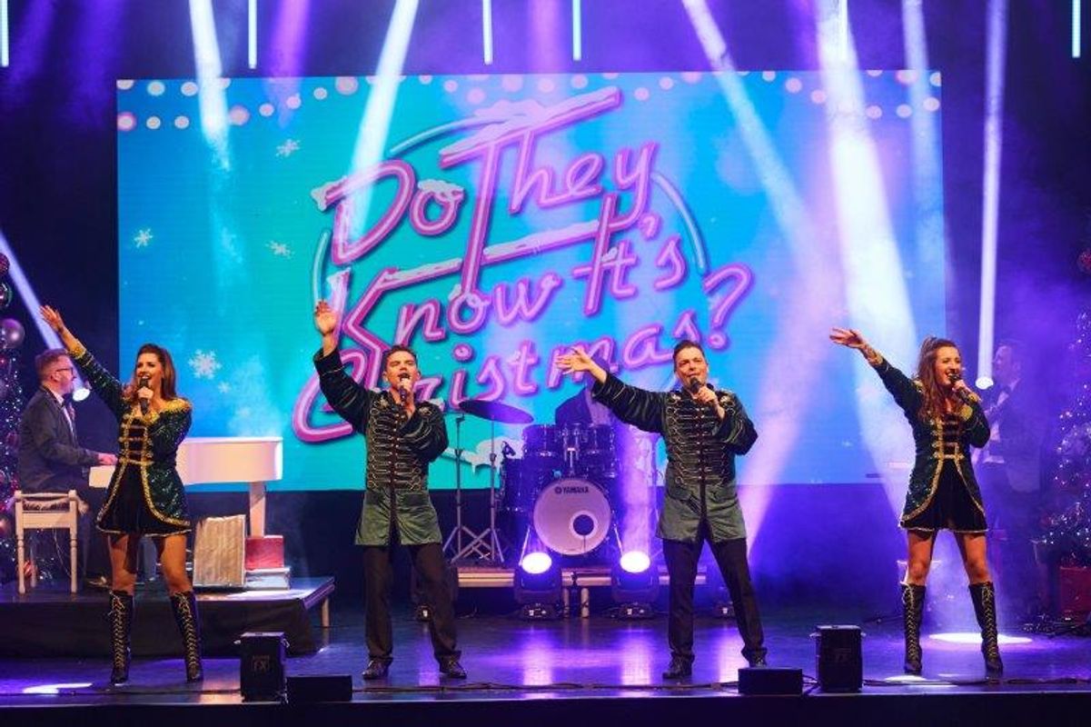 Four singers stand on stage wearing dark green outfits.