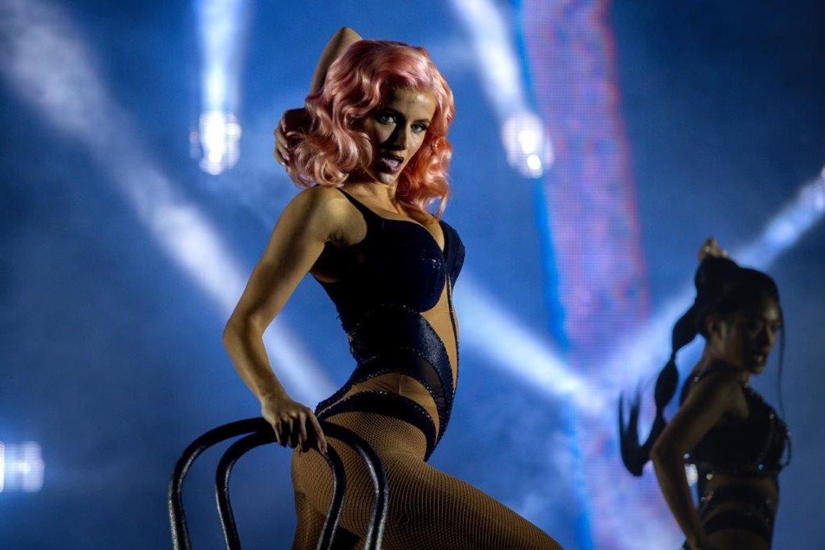 A lady in a pastel pink wig and corset and fishnets performing using a chair as a prop