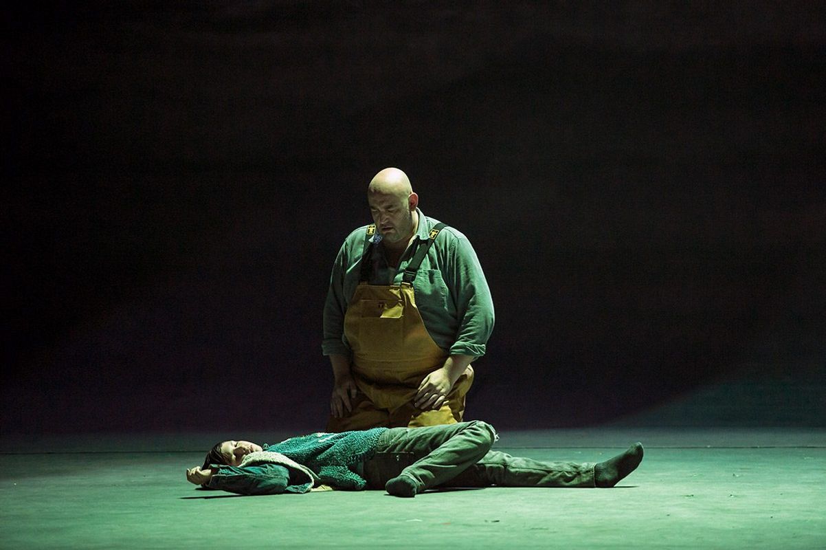 A person wearing yellow dungarees kneels over a lifeless body.