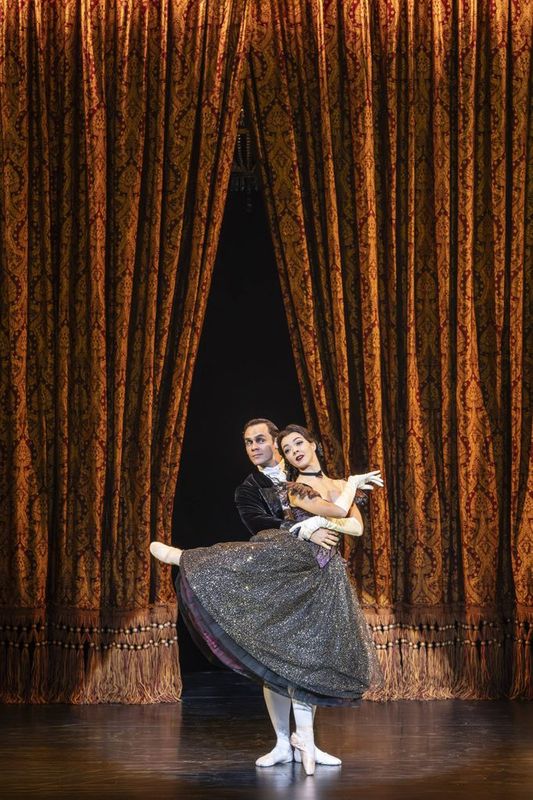 Two dancers duet in front of an open curtain.