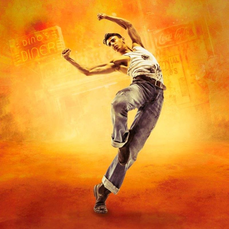 A dancer leaps energetically against a vibrant orange and yellow backdrop. He wears a white tank top and blue jeans, exuding confidence and dynamism. Neon diner signs are faintly visible.