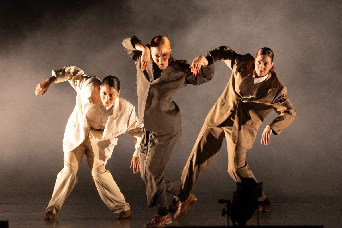 Three people dressed in neutral coloured suits  raises both arms in a hanging postion.
