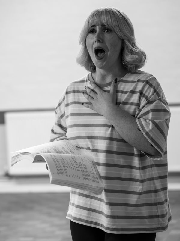A woman is gasping and has her hand on her chest, she is holding a script in the other