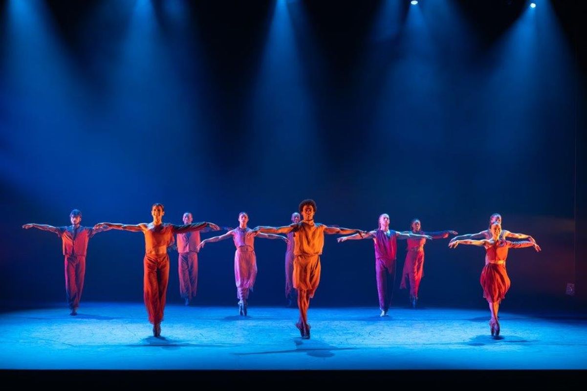 Group of dancers in orange and brown clothing with a soft spot light on them
