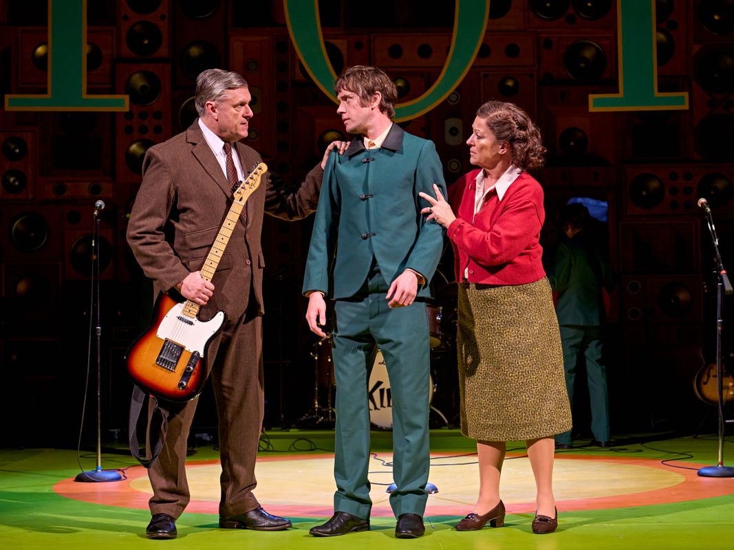 A person dressed in green is consoled by two older figures.