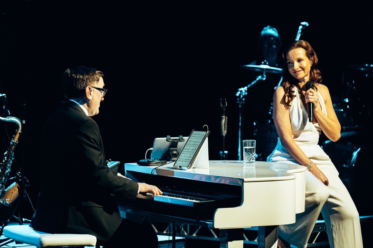 Two people sit around a white piano.