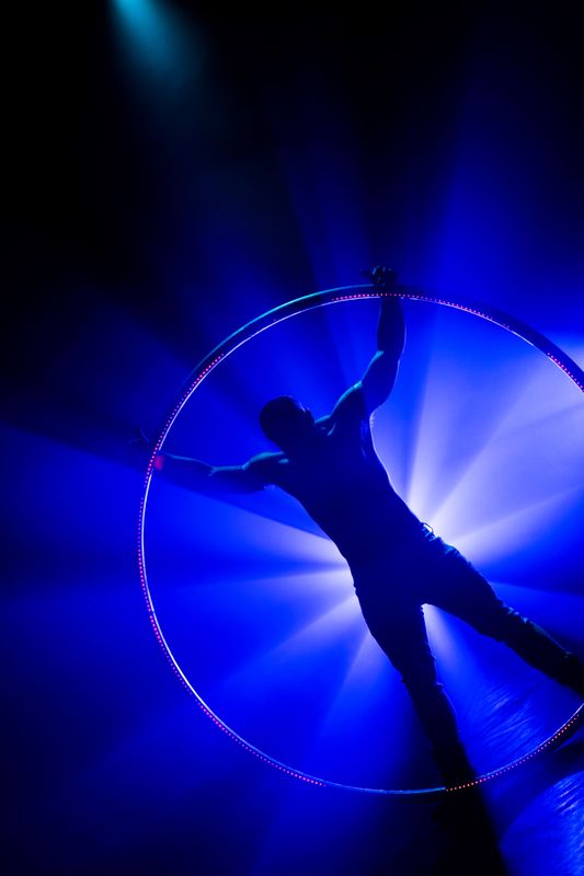 A circus performer stands in a starfish motion with a giant ring in front.