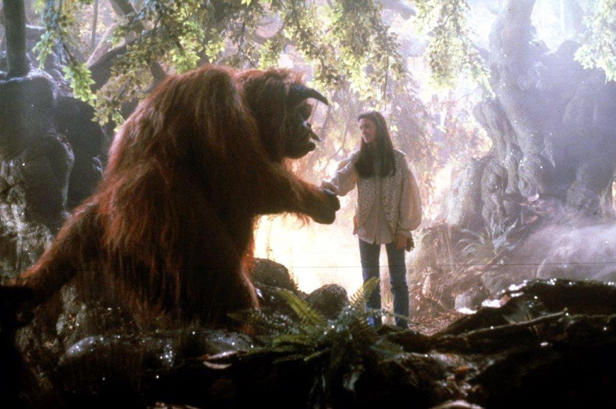 A person wearing a long flowy shirt holds hands with a giant hairy animal. 
