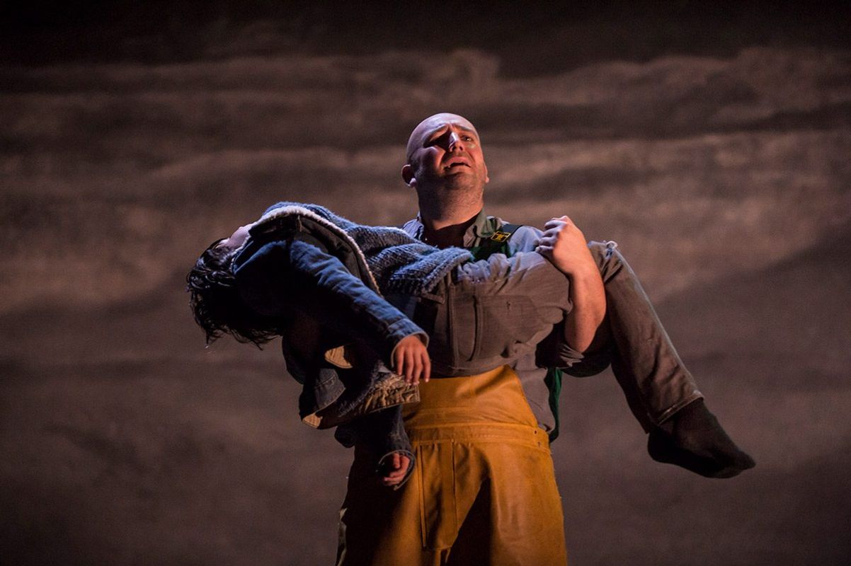 A person wearing yellow dungarees carries a lifeless body.