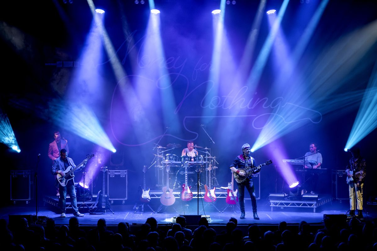 Band on stage performing, they're playing guitars and drums and there are flashing lights around them
