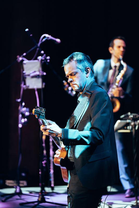 A person wearing a black blazer plays guitar.