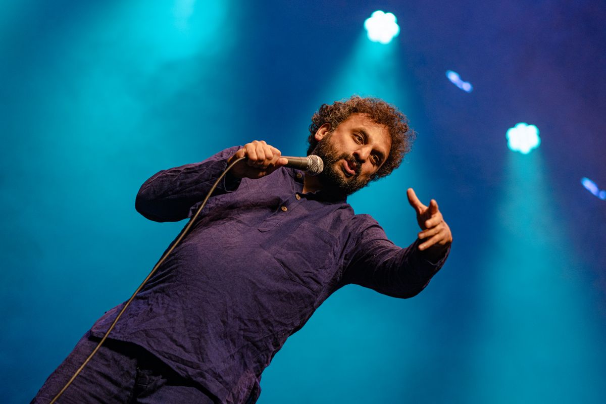 Nish stands onstage gesturing to the audience.