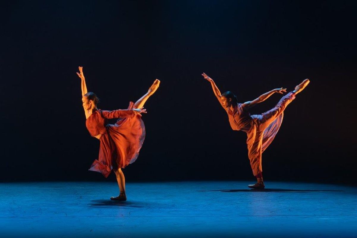 Two dancers with one of their legs up in the air behind them and their arms stretched out