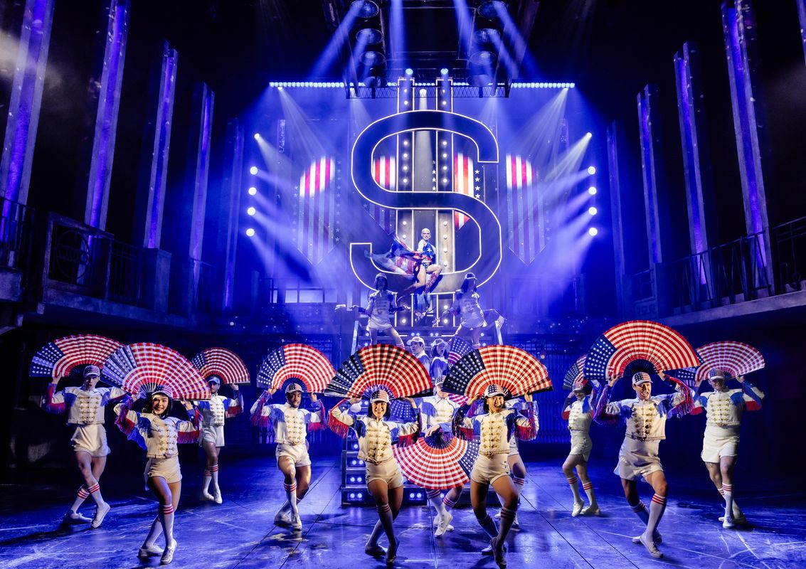 The ensemble dressed in white hold fans displaying the USA flag above their heads.