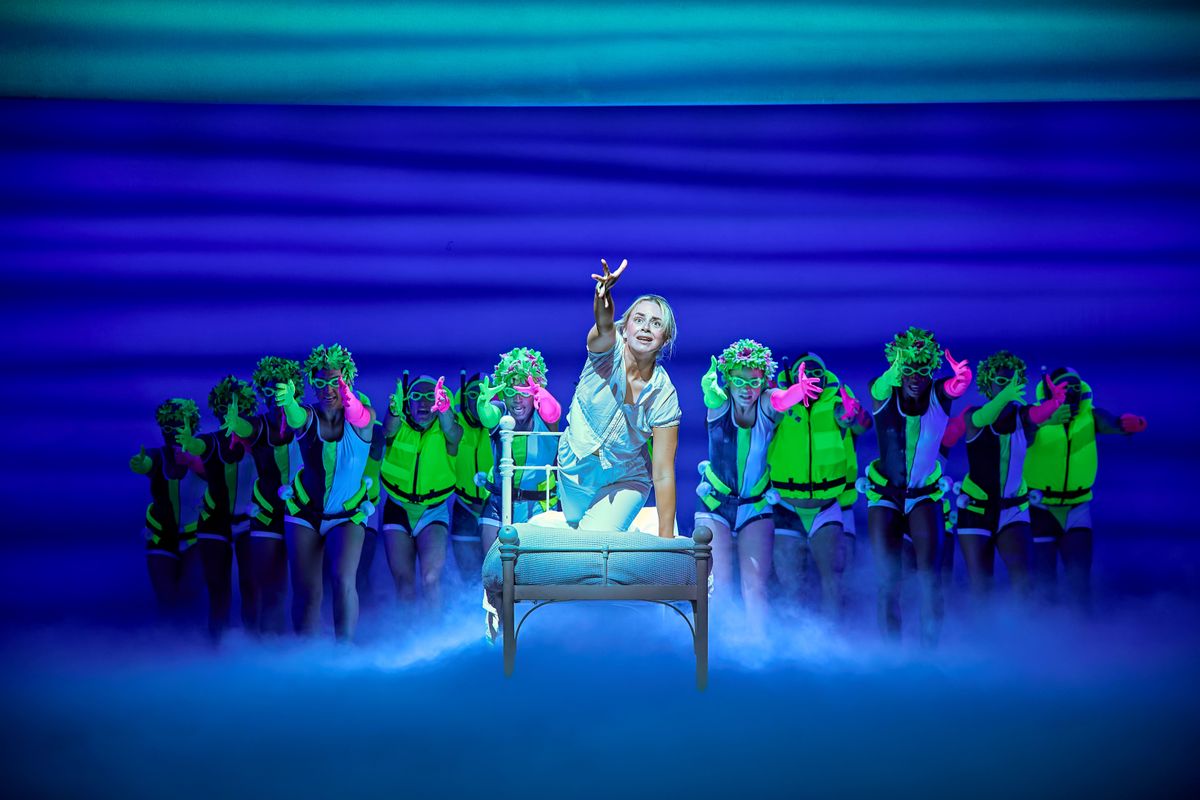 Sophie kneels on a bed surrounded by the ensemble wearing neon life jackets.
