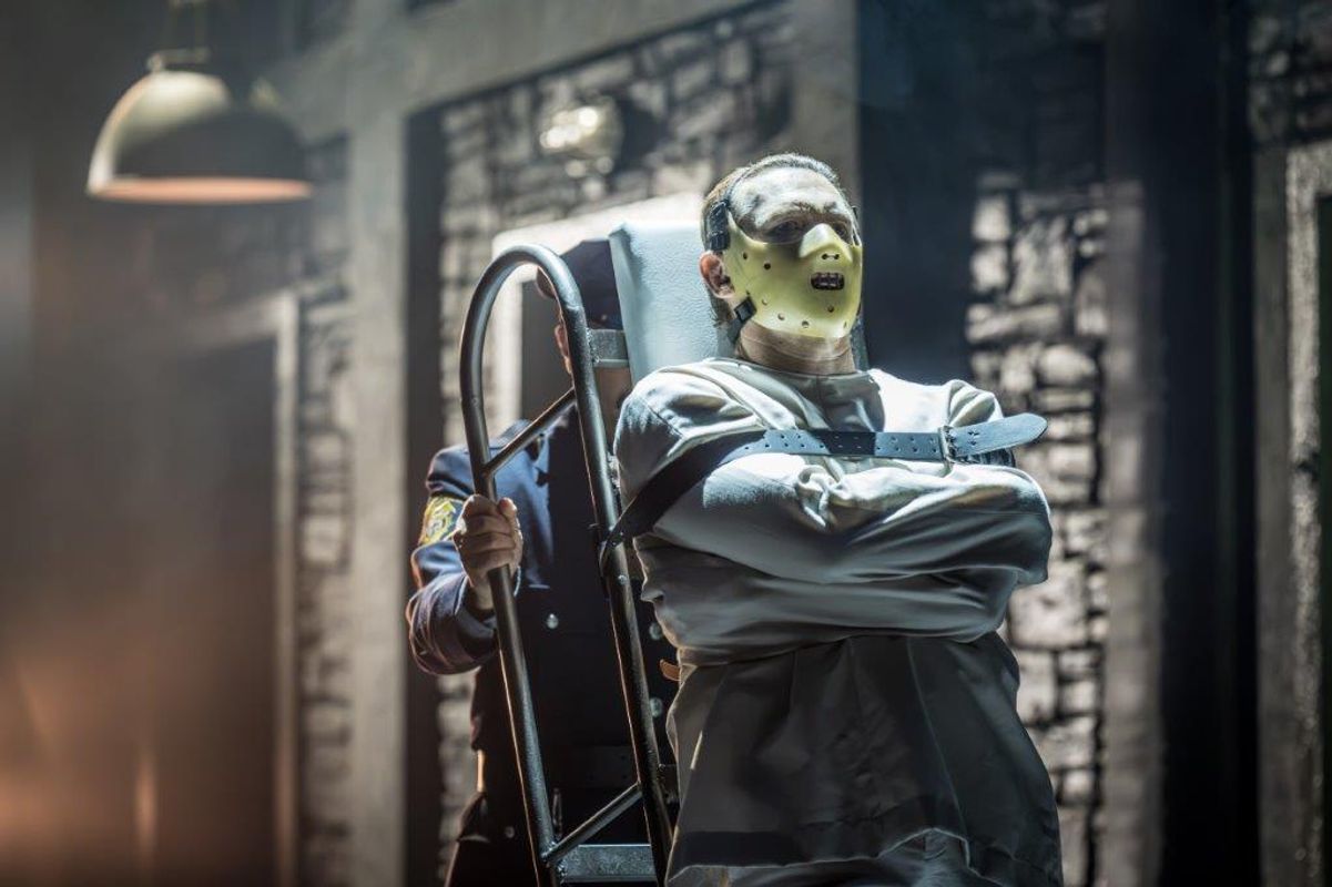 A man is strapped to a gurney and is wearing a straight jacket and a mask that covers the bottom half of his face