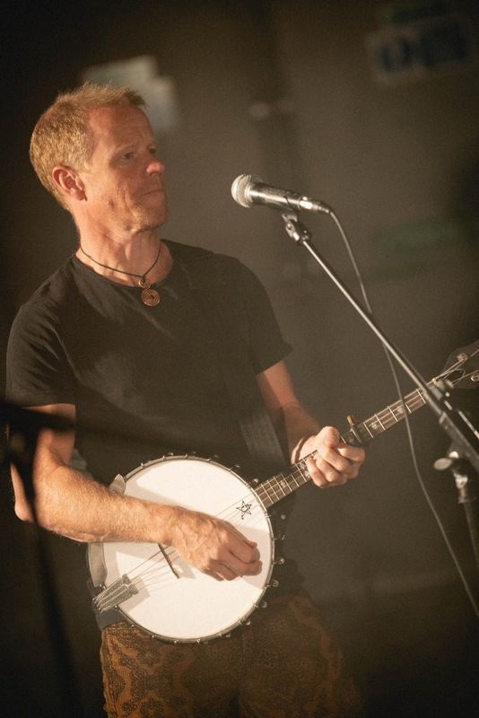 Musician playing a banjo on stage near a microphone.