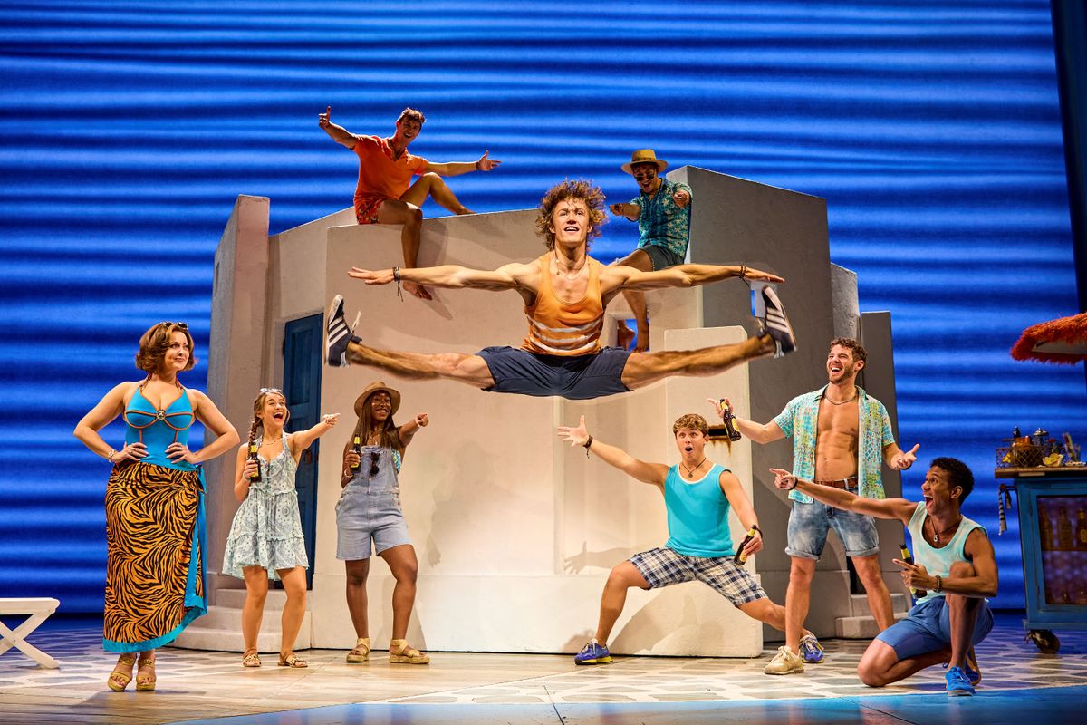 A person does a split jump in the air with other people watching.