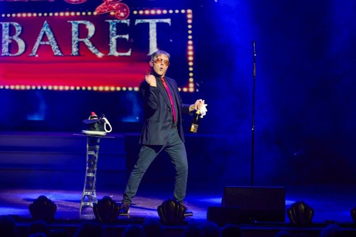 A person wearing a black suit holds a bottle of champagne.