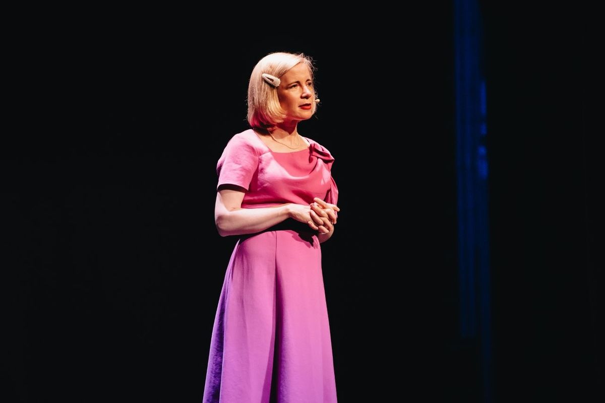 Lucy Worsley talking on stage. She is wearing a pink dress.