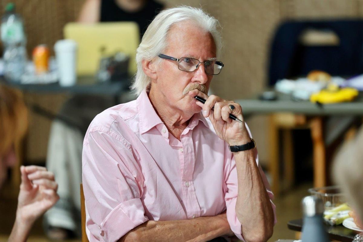 A man wearing glasses and holding a pen, he looks deep in thought