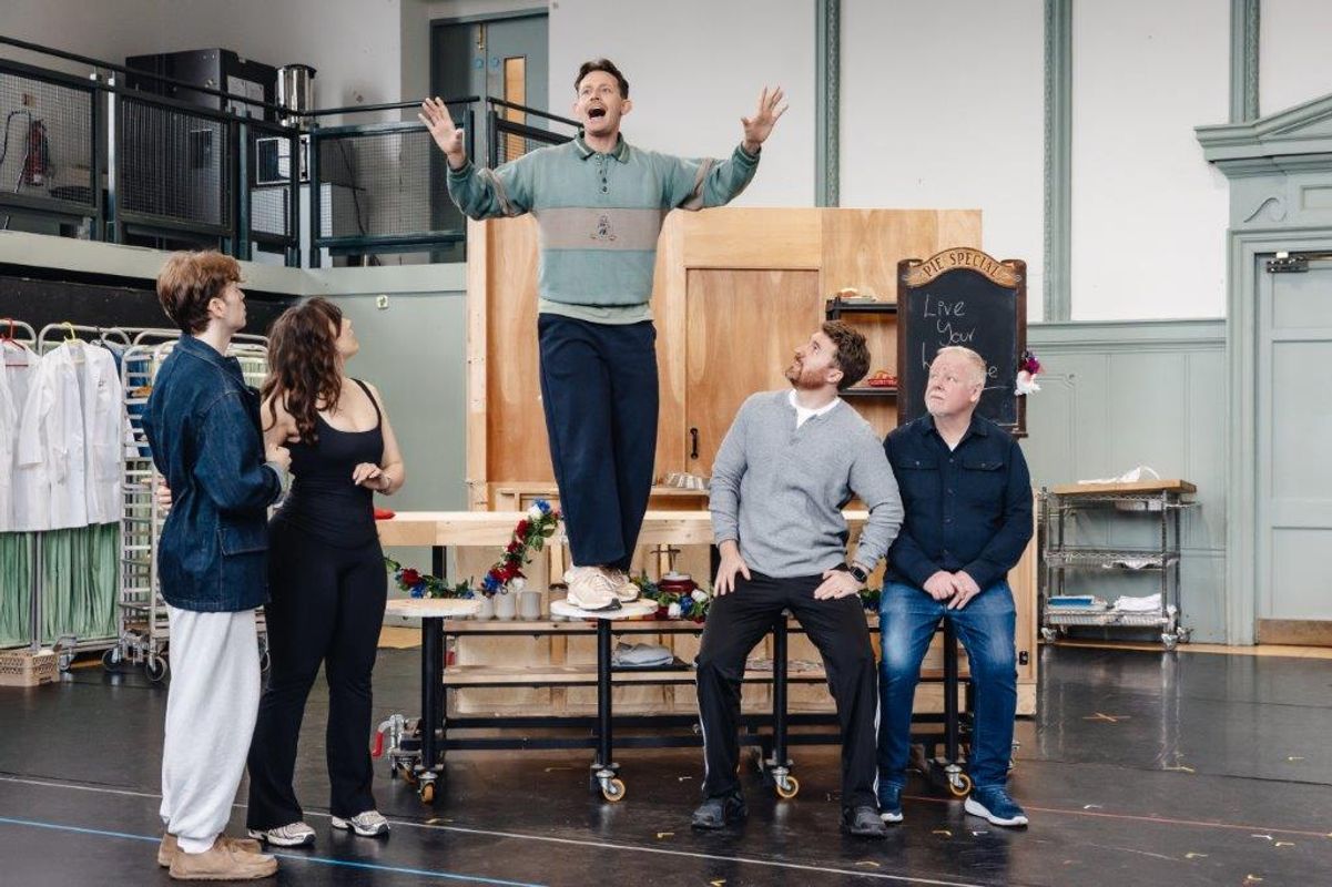 A person is stood on a table and four other people are stood around it watching