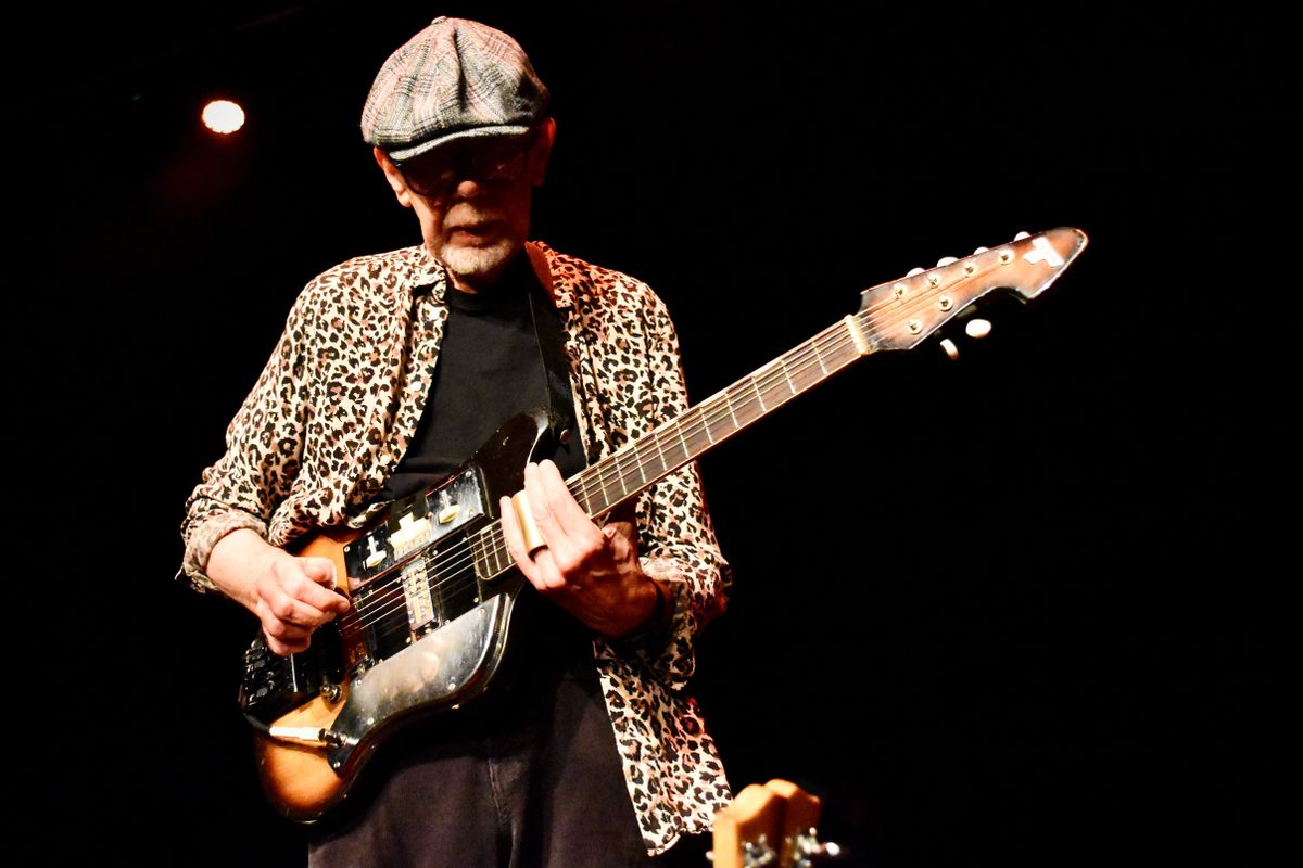 A person in a leopard print shirt plays guitar.