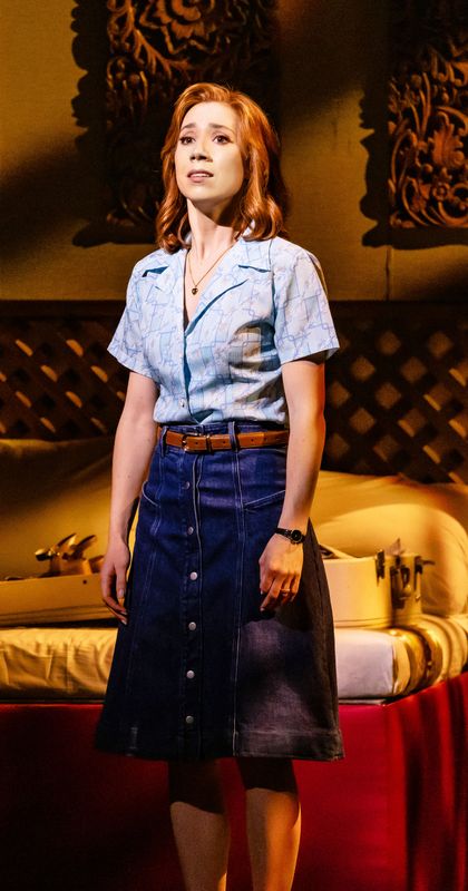 A person dressed in a denim skirt and light shirt looks pensive.