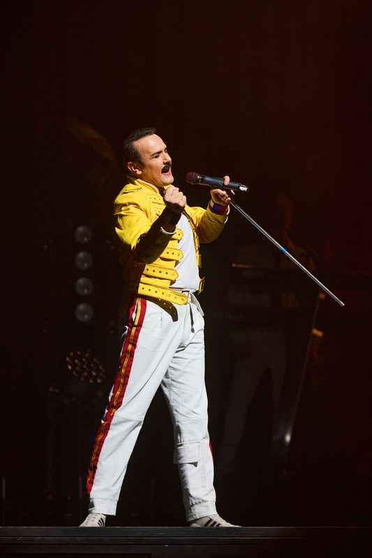 A man performing in a yellow jacket on stage and holding a microphone
