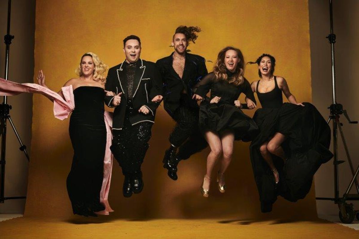 Five people jumping joyfully against a yellow background, wearing elegant black outfits. Their expressions convey excitement and energy.